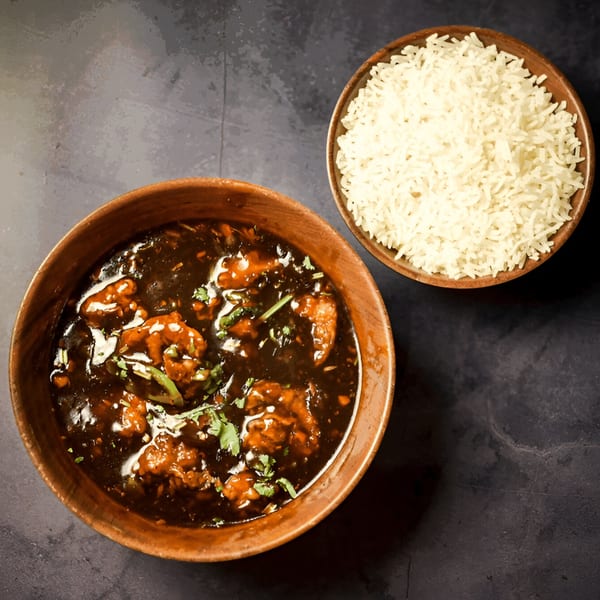 Indian chili chicken with dark sauce and white rice in wooden bowls on a dark surface.