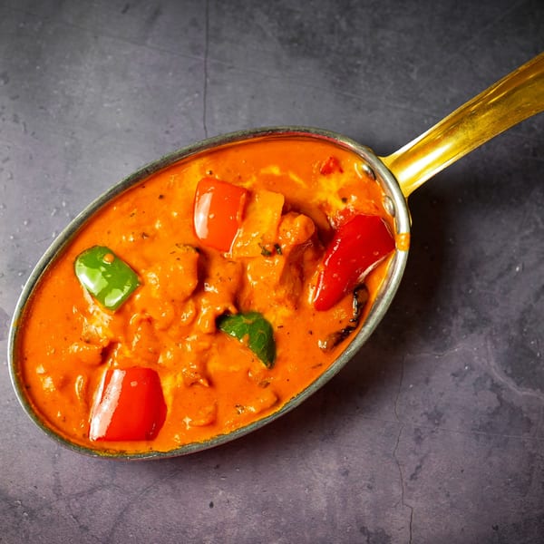 Overhead view of Indian curry with red and green bell peppers in a golden serving dish.