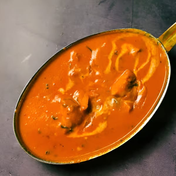 A close-up of The Monk's Indian Bistro's butter chicken, a rich orange curry with cream swirls.