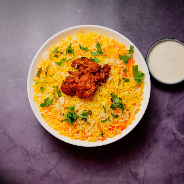 Chicken biryani with cilantro and a side of raita, presented on a dark surface.