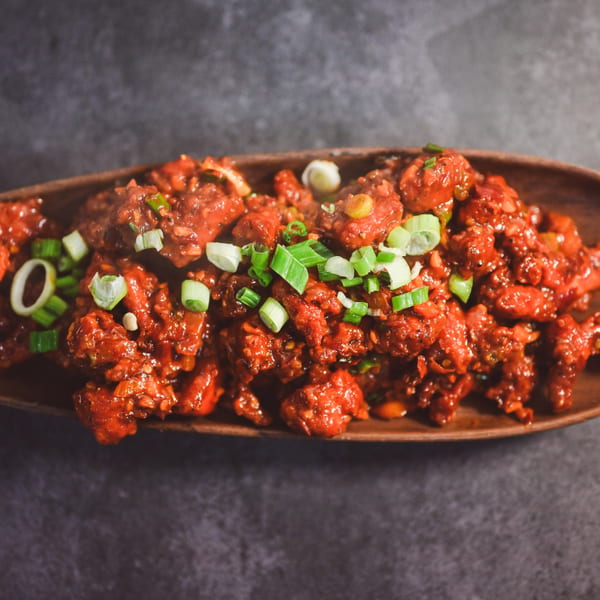 A close-up of The Monk's Indian Bistro's chili chicken, garnished with fresh green onions.